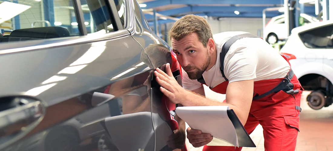 Mann prüft ein Auto für Smart Repair und schaut auf anfallende Dellenentfernung